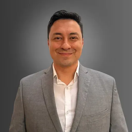 Smiling person in a gray blazer and white shirt against a dark gray background