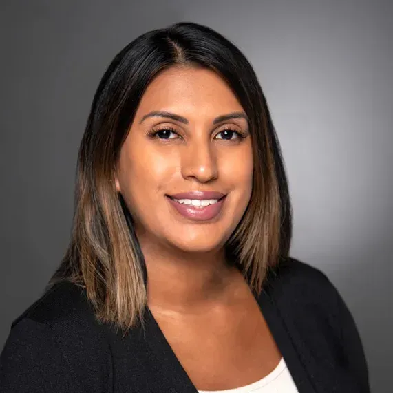 Headshot of a smiling person in a black blazer against a gray background