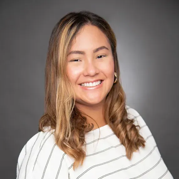 Smiling person with wavy hair in a white striped shirt against a gray background