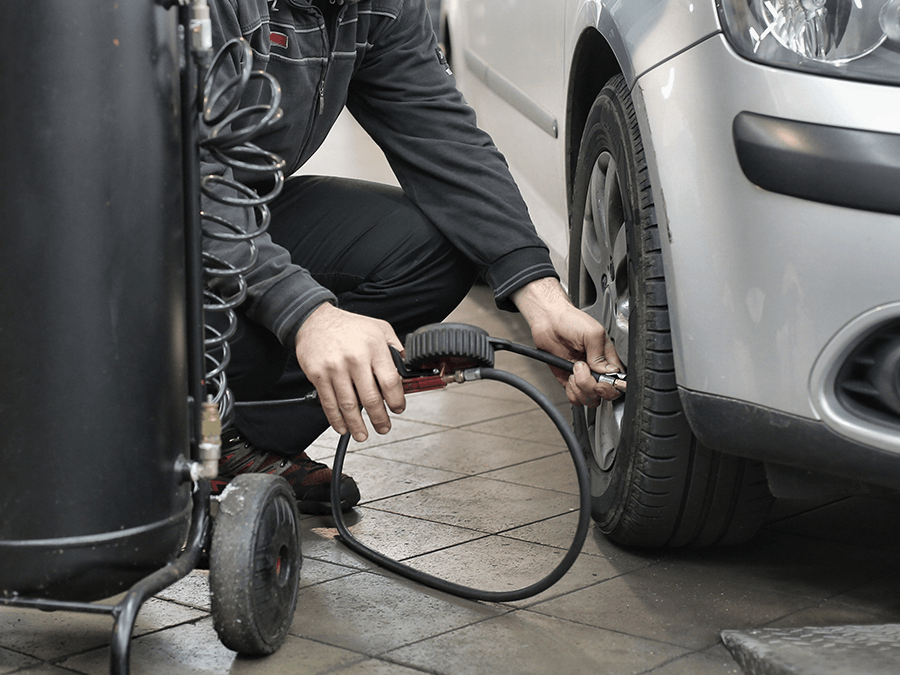A man is kneeling down to inflate a tire on a car.
