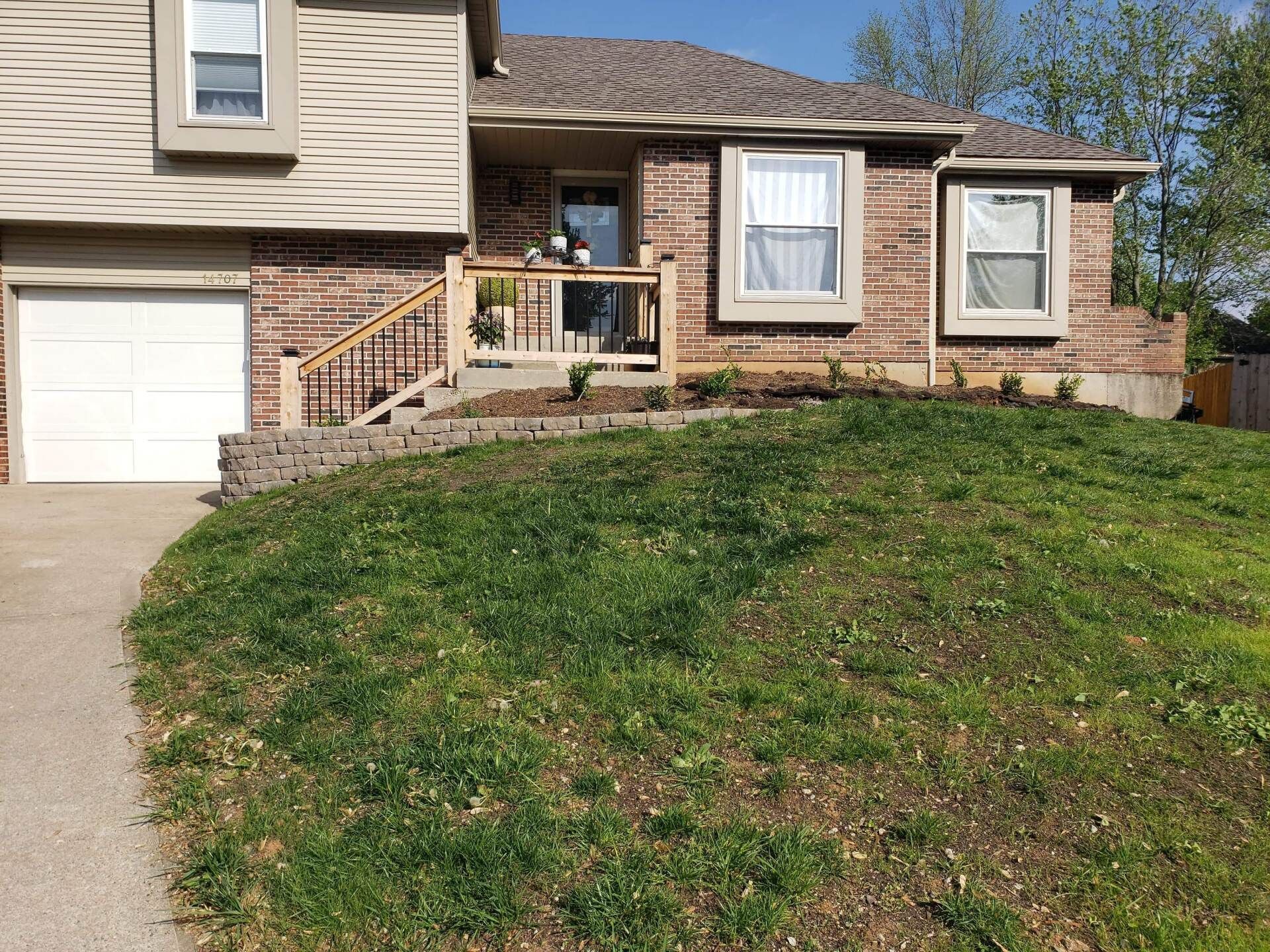 Suburban house with beige siding, brick front, garage, and steep grassy front yard.