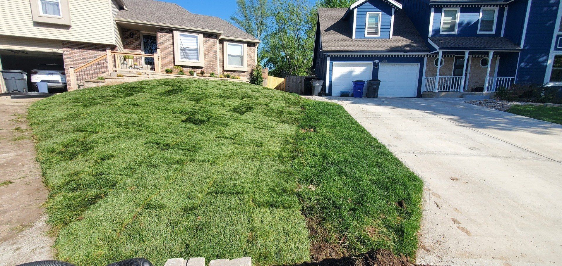 Suburban house with a steep grassy front lawn beside a driveway and garage