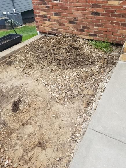 Pile of dirt and gravel beside a brick wall next to a concrete sidewalk