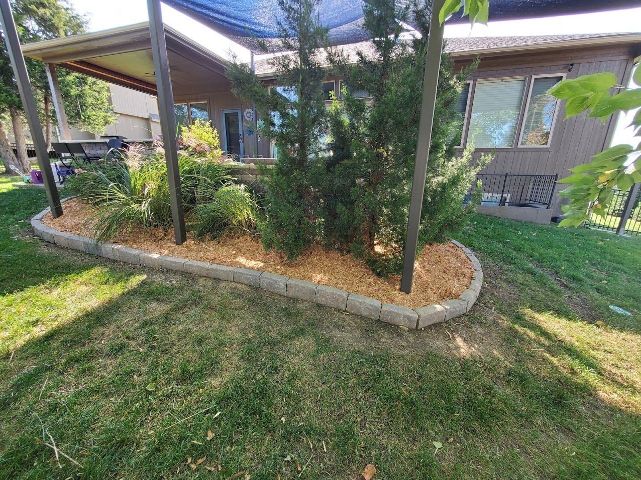 Shaded front yard with curved stone planter, trees, and a brick house porch