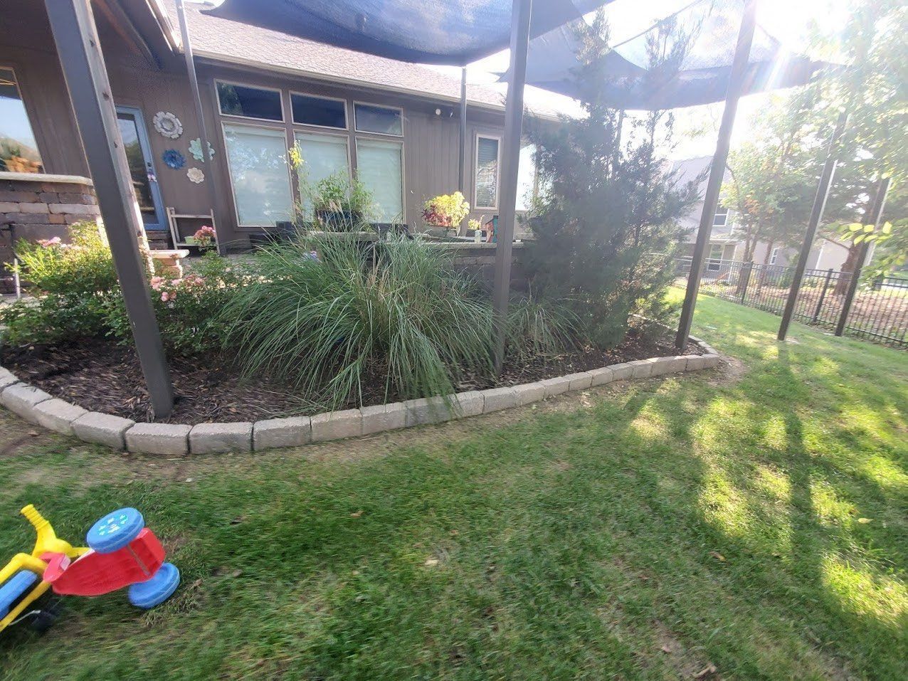 Sunny backyard with lawn, garden bed, patio, and a child’s toy in the foreground