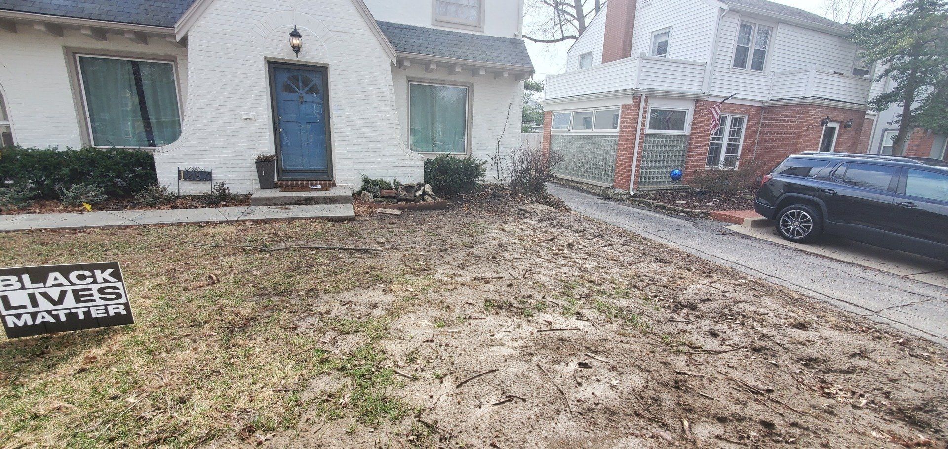 Front yard with a wet lawn, “Closed” sign, white house, and parked car on a rainy day