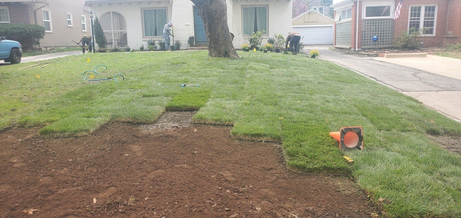 Patchy front lawn with a bare dirt area and a small orange toy on the right near a house driveway.