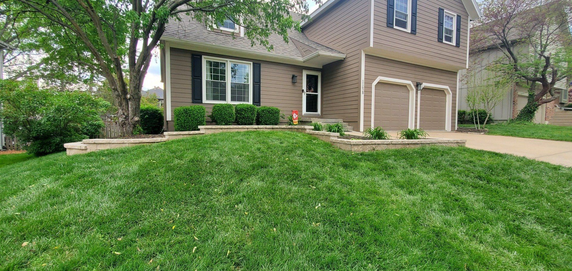 Brick suburban house with front lawn, beige garage doors, and landscaped entryway