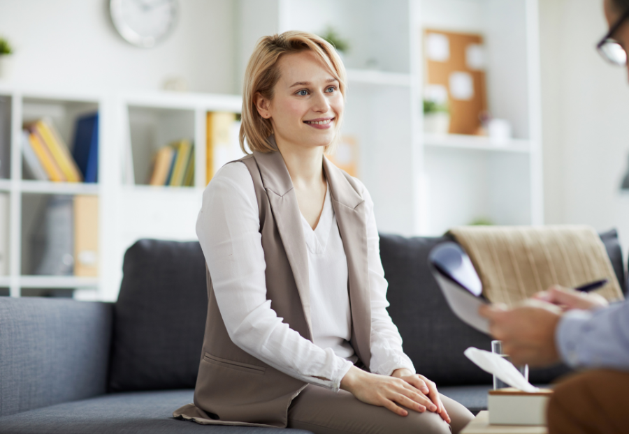 A picture of a woman smiling on a sofa while talking to someone across from her.