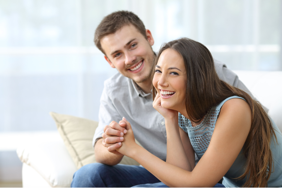 A picture of a couple holding hands laughing on a sofa.