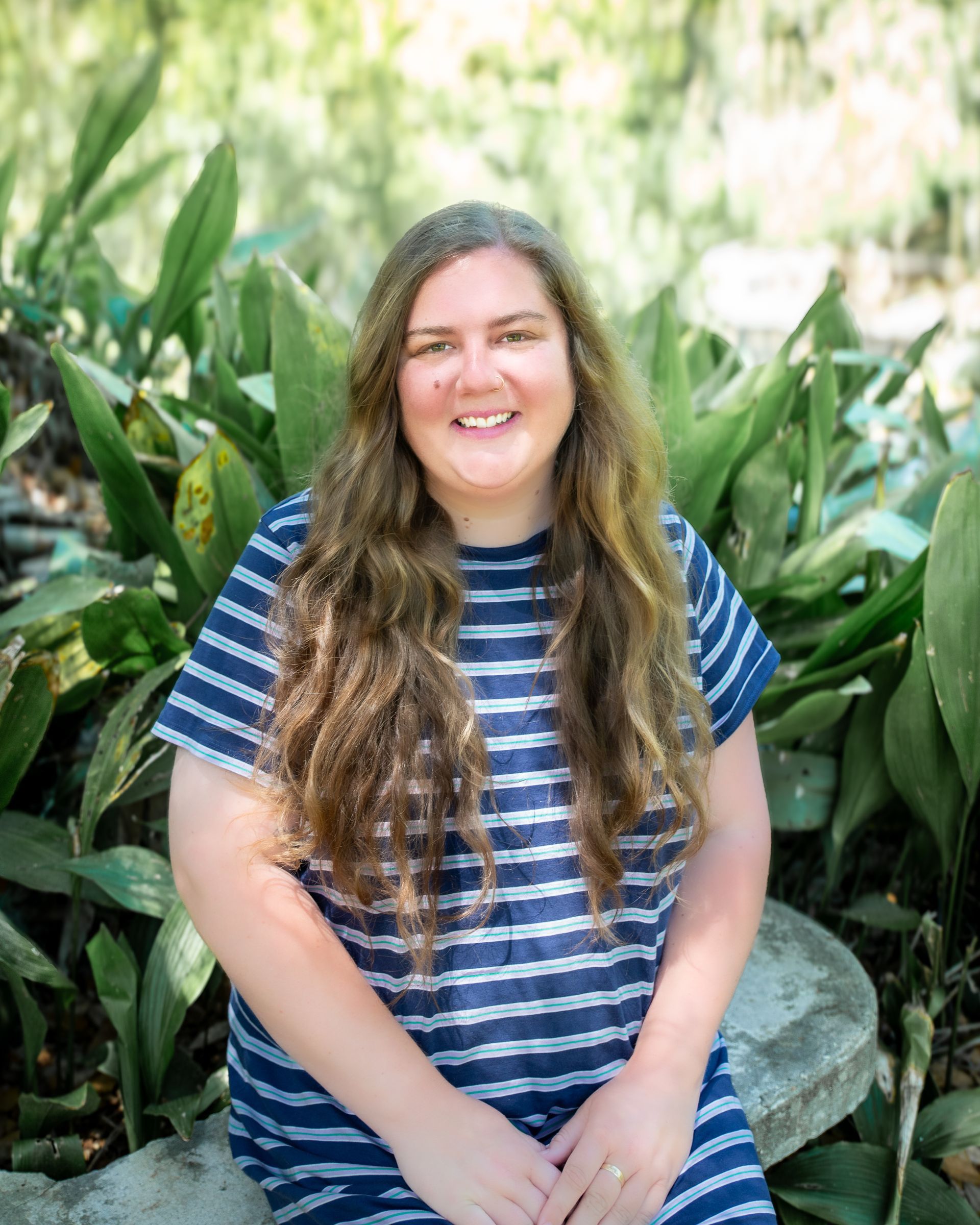Smiling person in a blue striped shirt standing among lush green plants outdoors