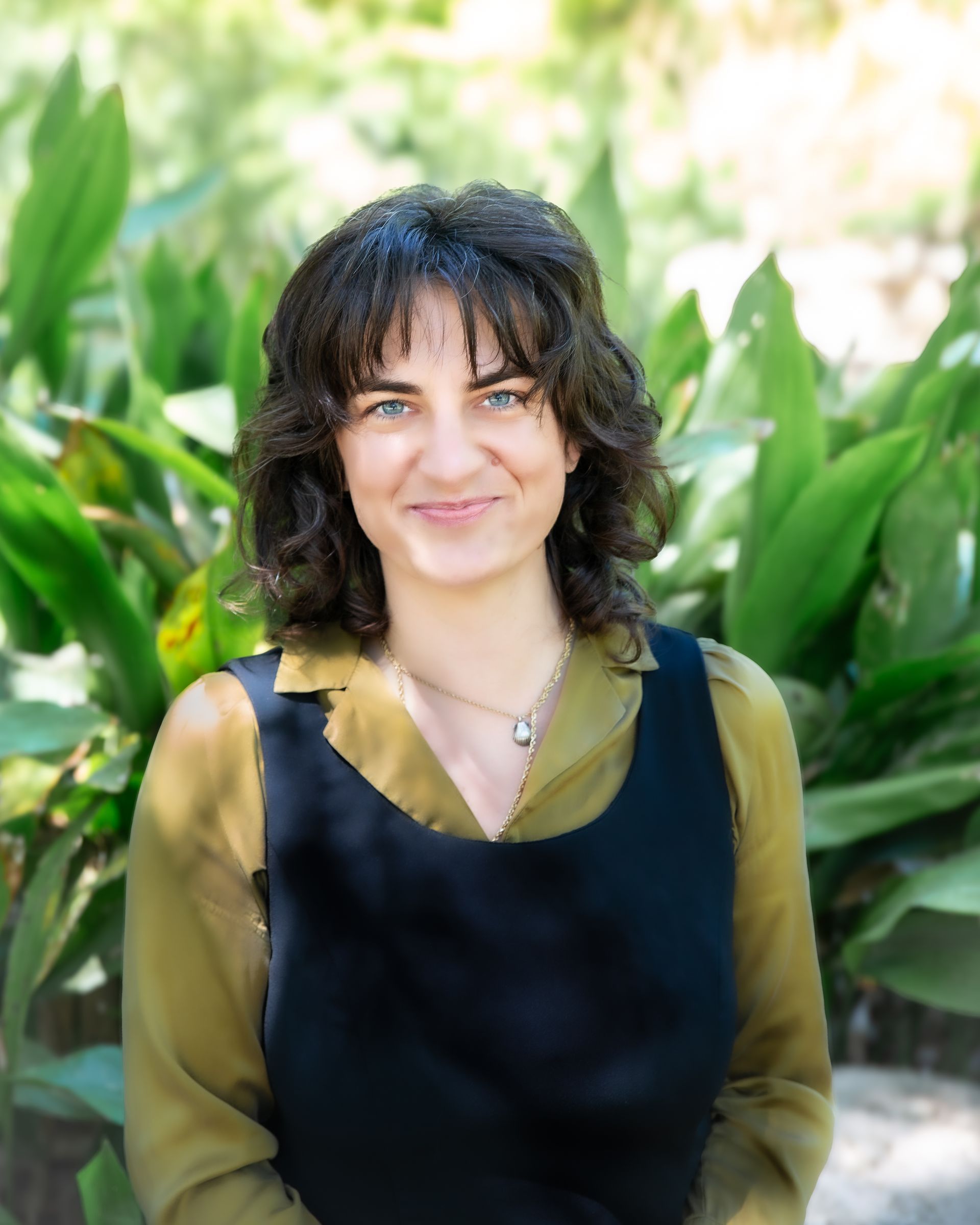 Woman smiling, wearing black jacket over ruffled top, outdoors.
