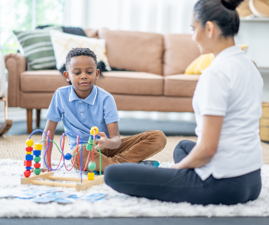 A picture of a little boy sitting on the ground playing with toys with an adult.
