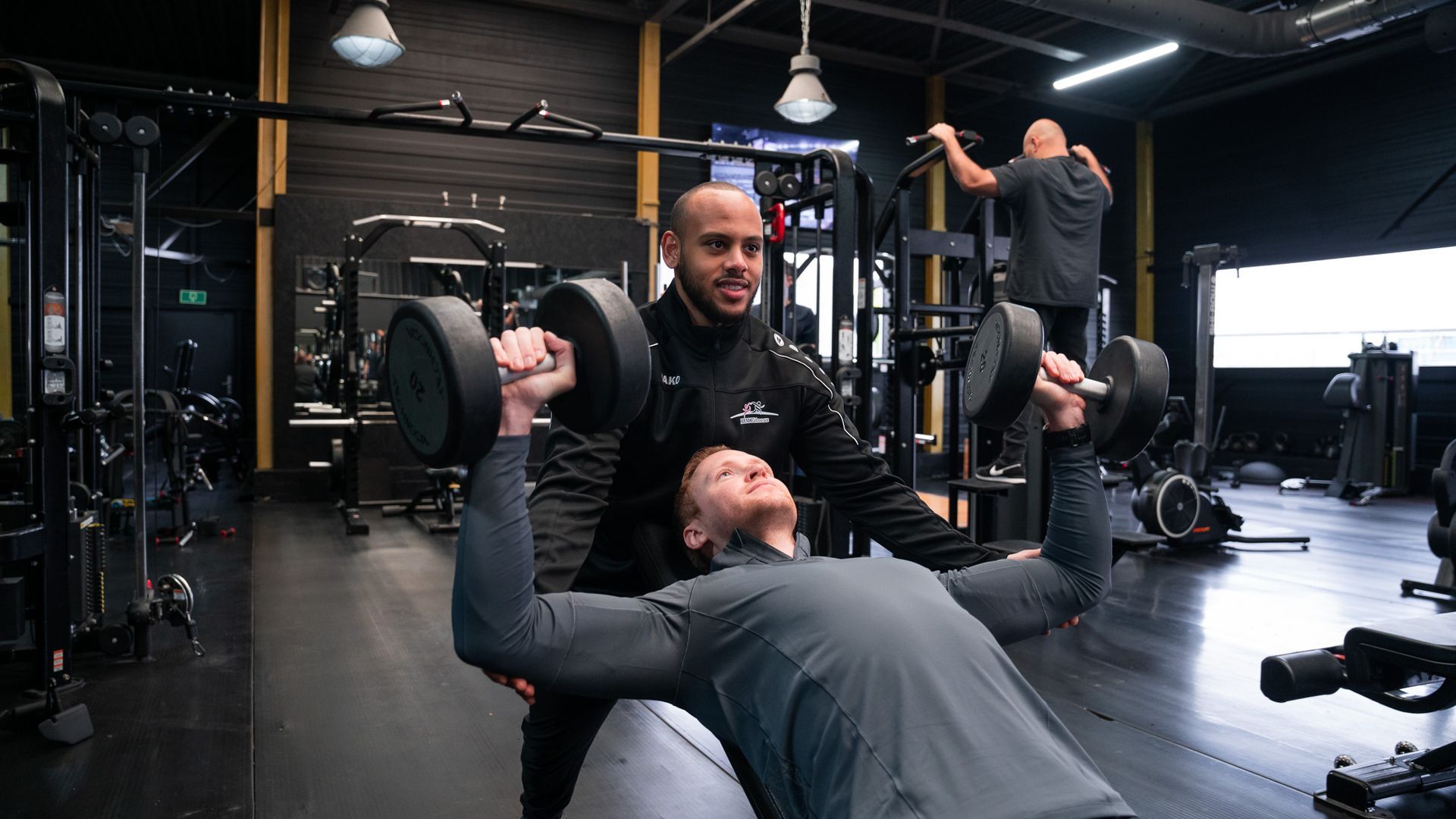 Man die bankdrukt en door een personal trainer wordt gespot in de sportschool.