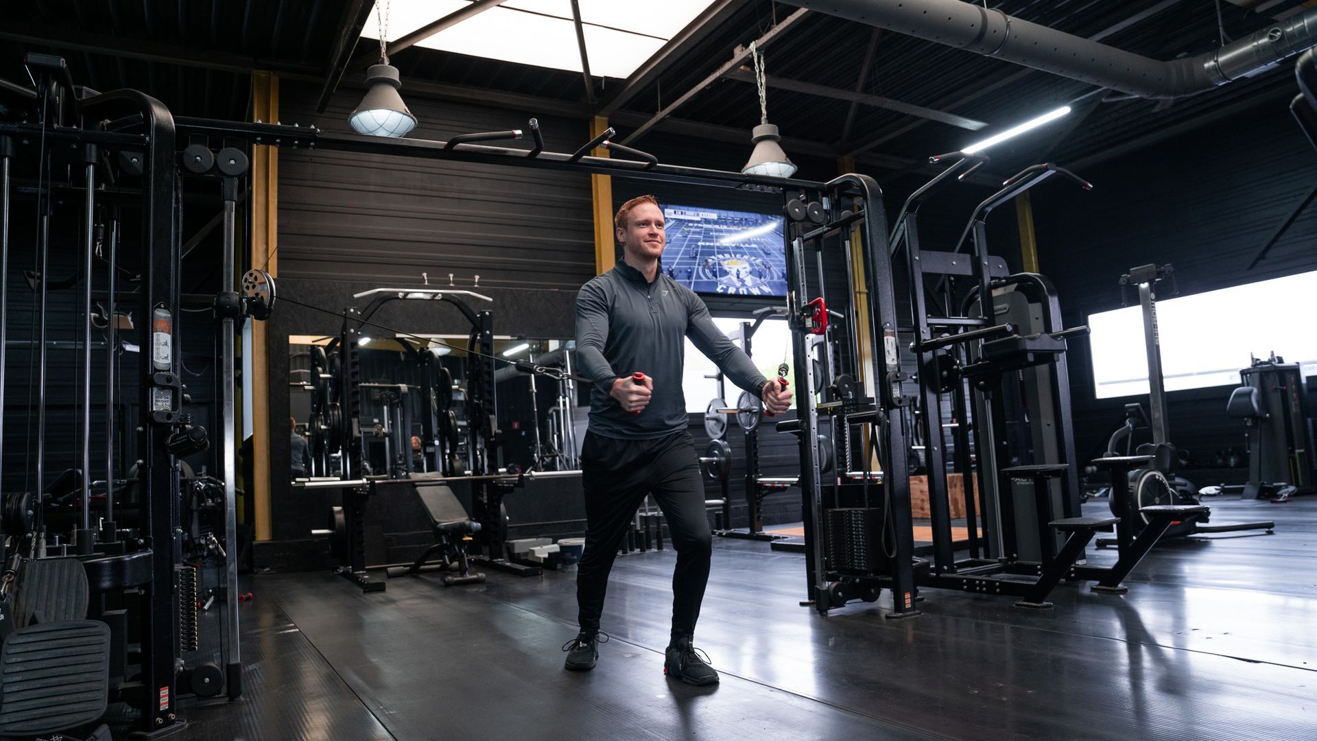 Een man is aan het trainen met een kabelmachine in een sportschool, met gestrekte armen.