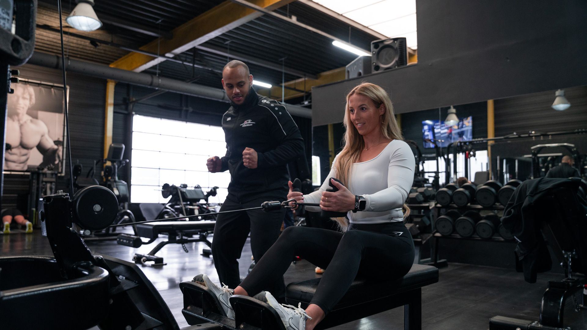 Vrouw traint op een roeimachine met een trainer in de sportschool.