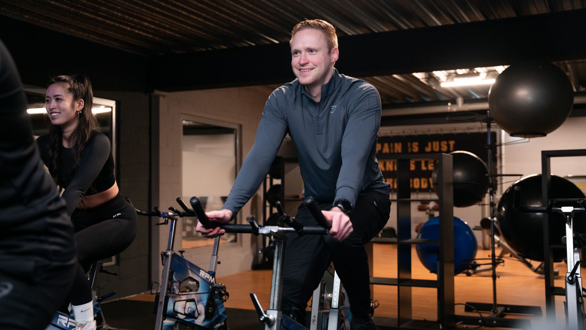 Een lachende man fietst met anderen op een hometrainer in de sportschool.