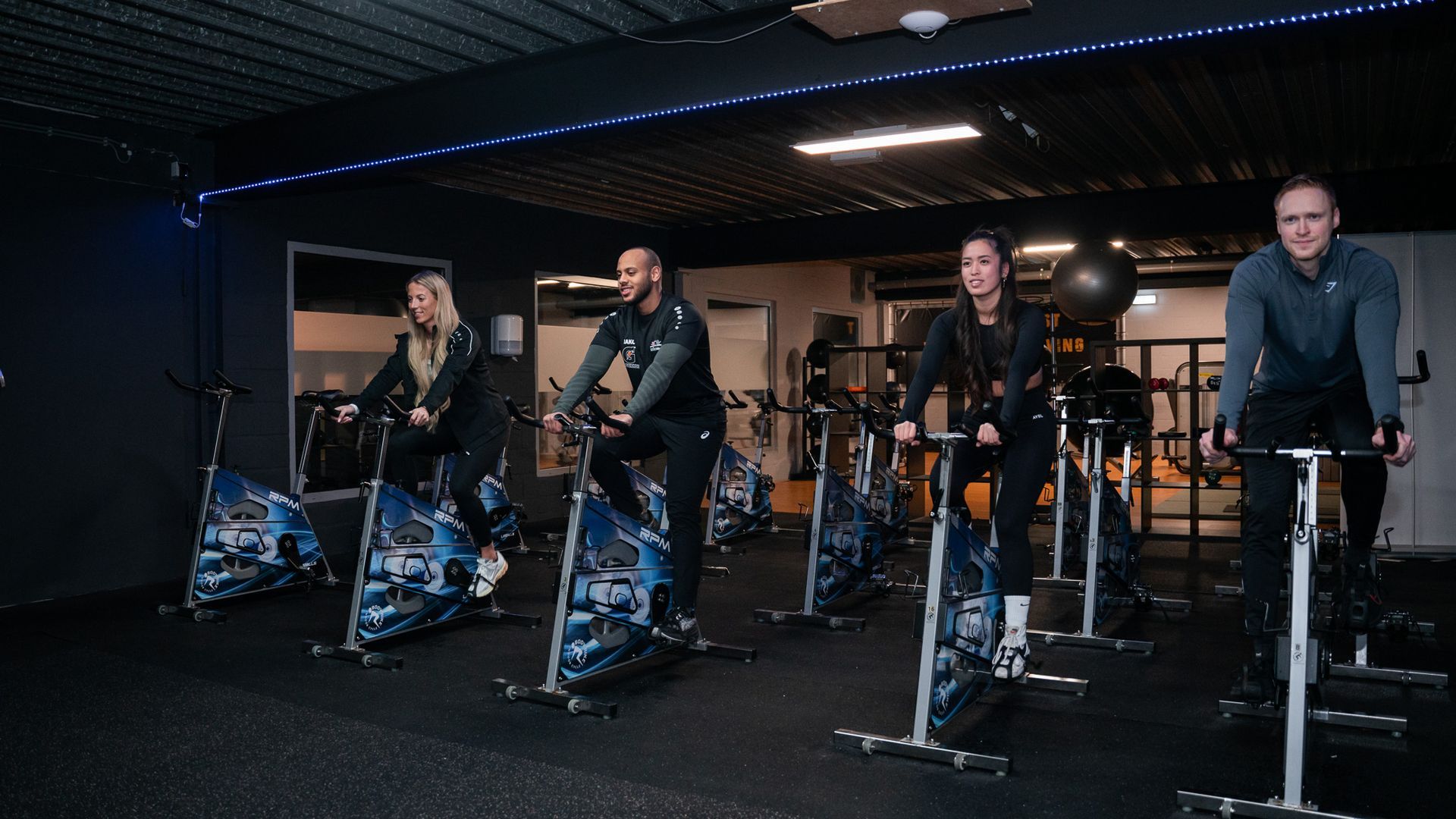Een groep mensen fietst op een hometrainer in een sportschool.