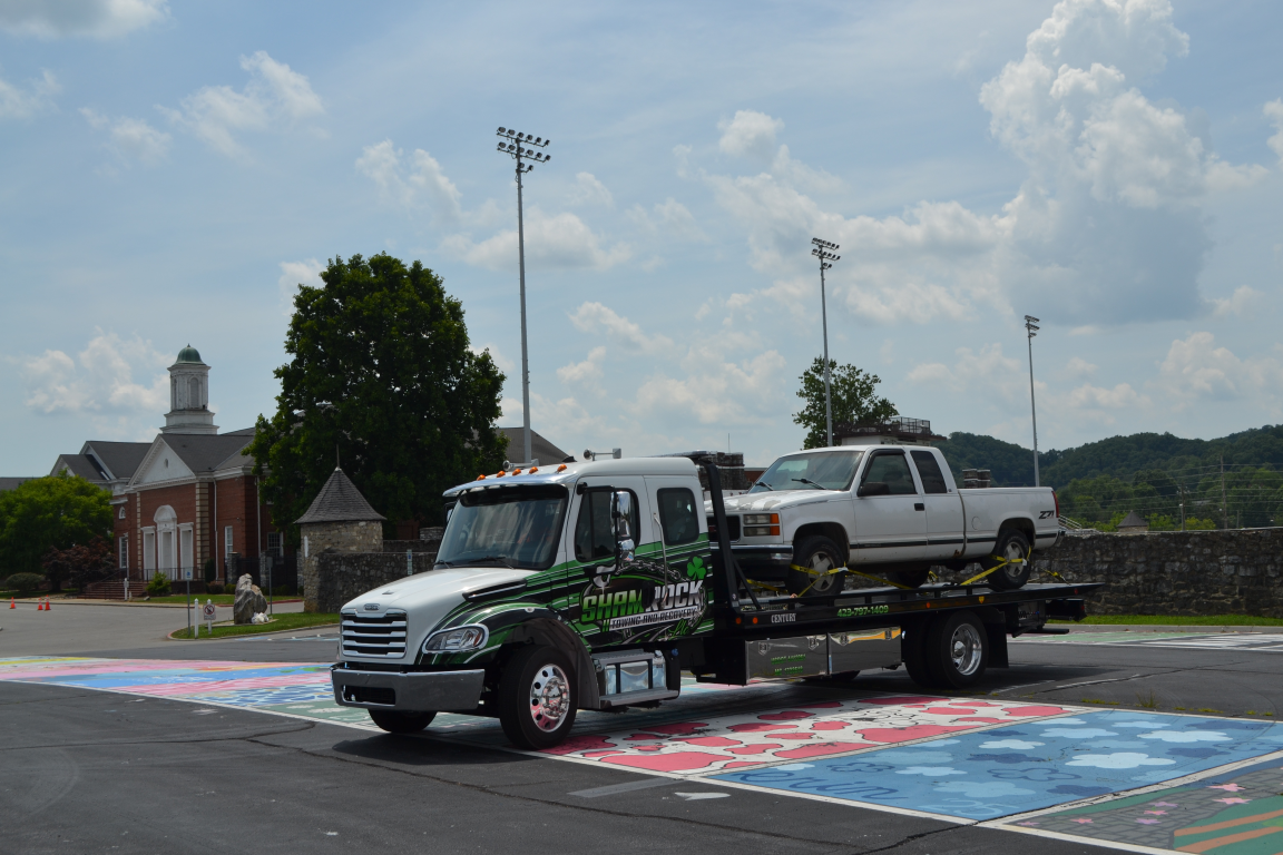 Tow truck hauling a white SUV on a flatbed truck in a parking lot under a cloudy sky
