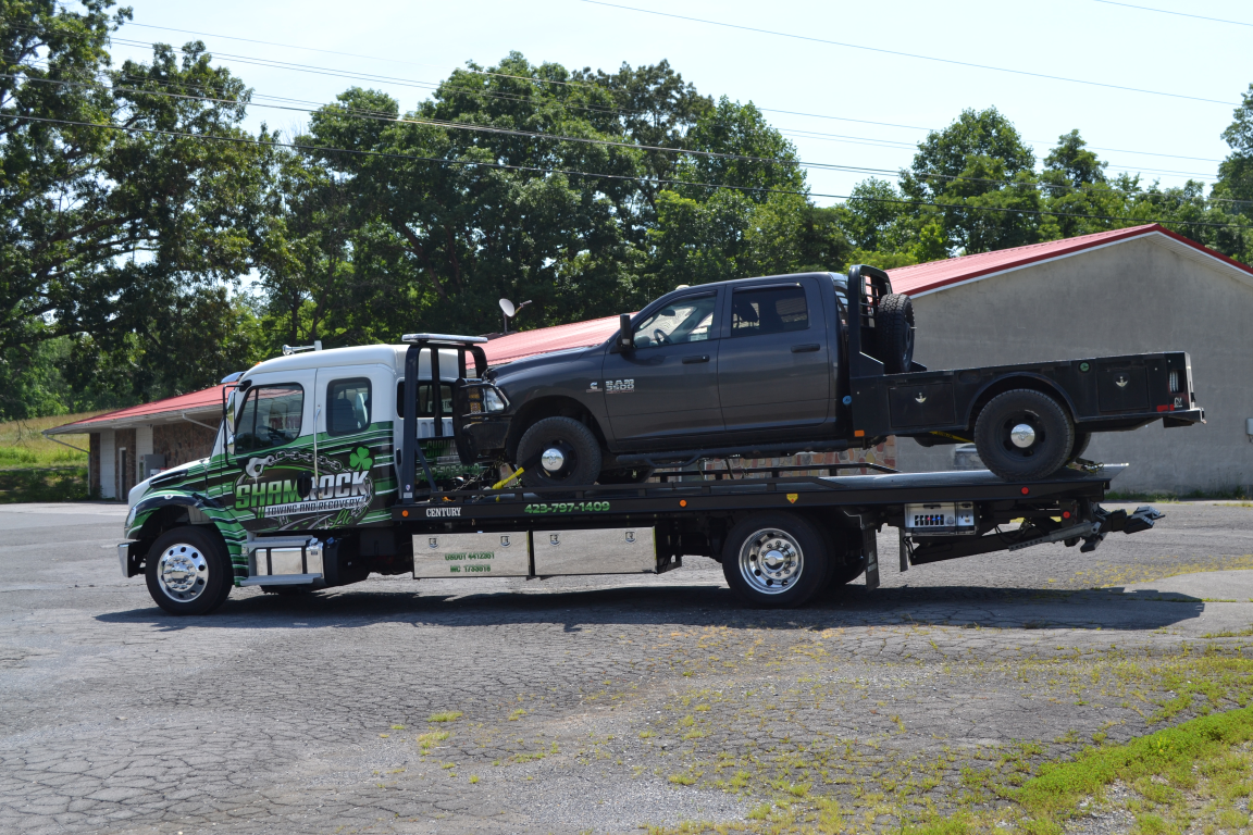 Tow truck carrying a black pickup on a flatbed trailer in a parking lot