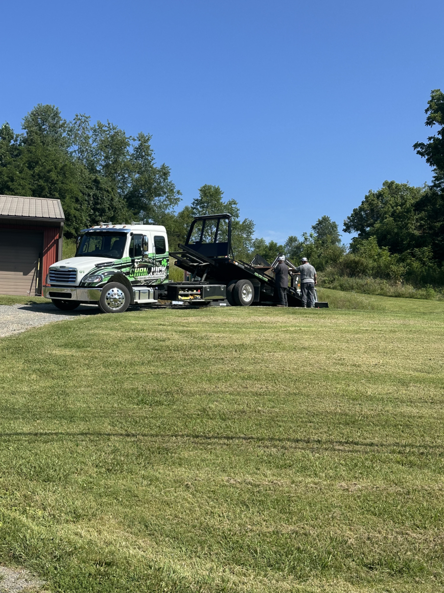 Tow truck and small SUV beside a building on a grassy field under a clear blue sky