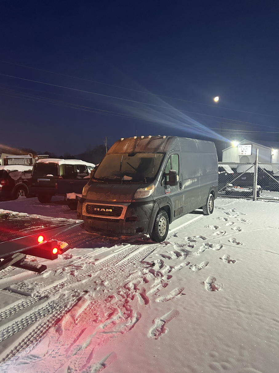 Snowy parking lot at night with a gray van parked beside other vehicles and red lights glowing nearby