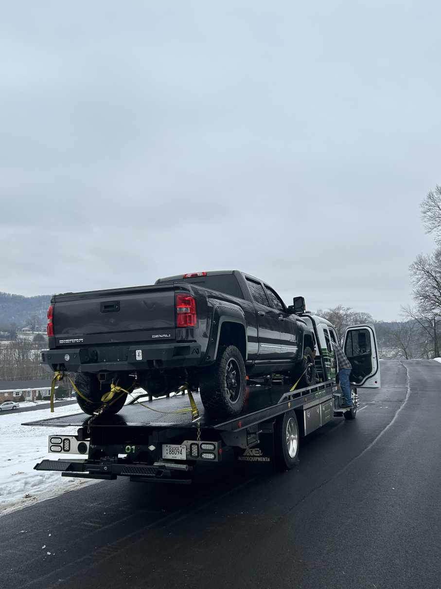 Black pickup truck loaded on a tow truck driving on a snowy roadside