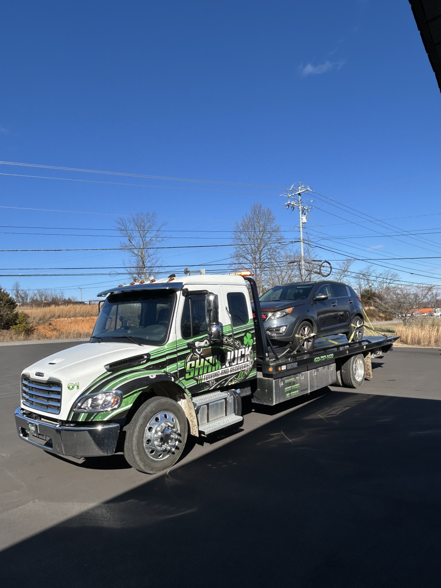 Tow truck carrying a black SUV on a clear day, parked on pavement under a blue sky