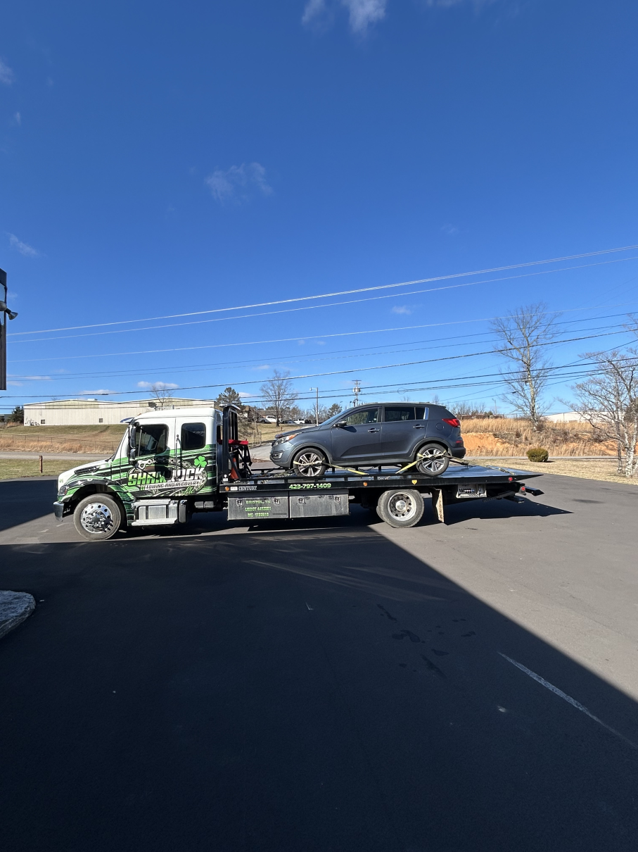 Car carrier truck hauling a black SUV in a sunny parking lot under a clear blue sky