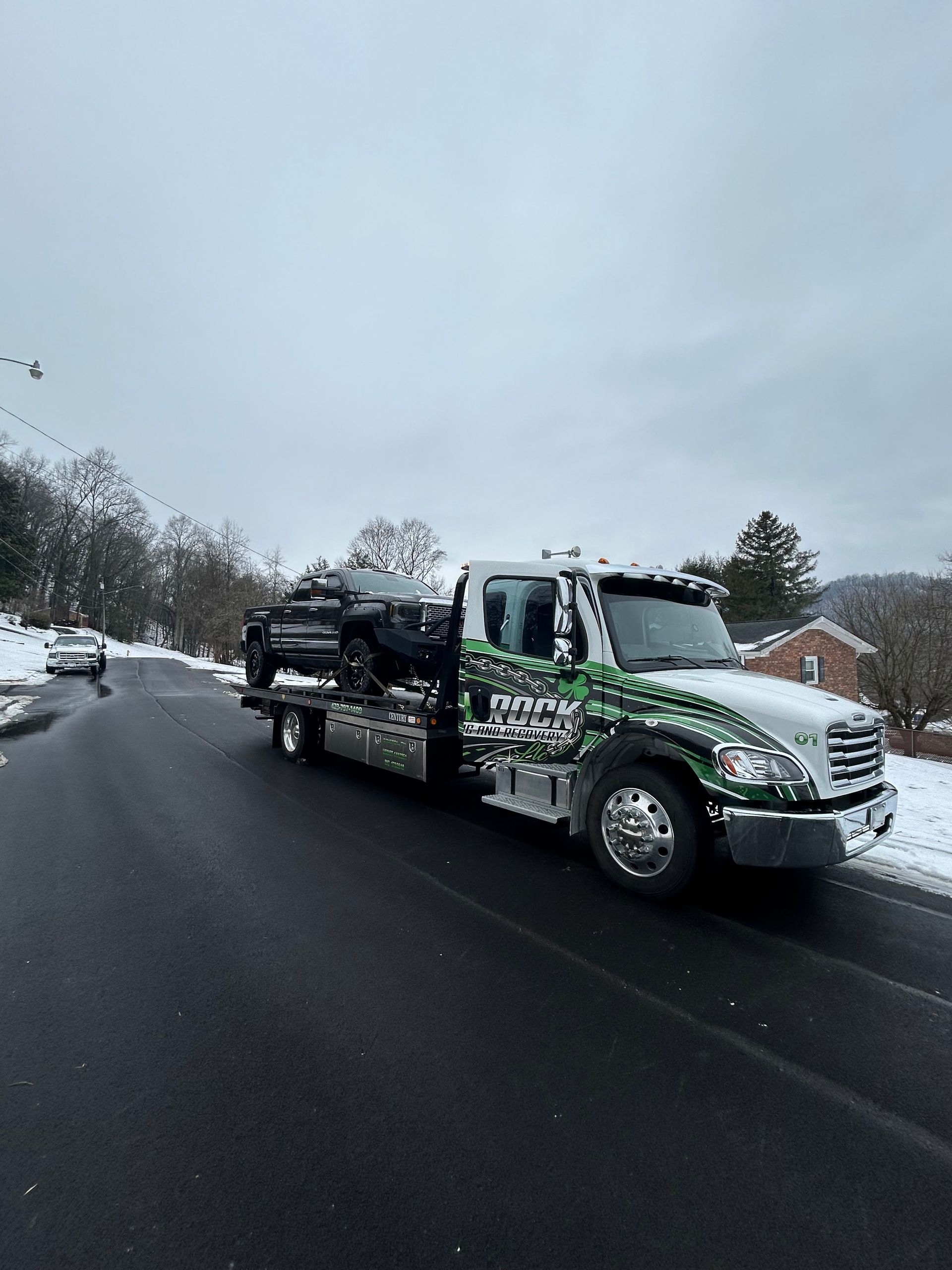 Tow truck hauling a black car on a snowy road under an overcast sky