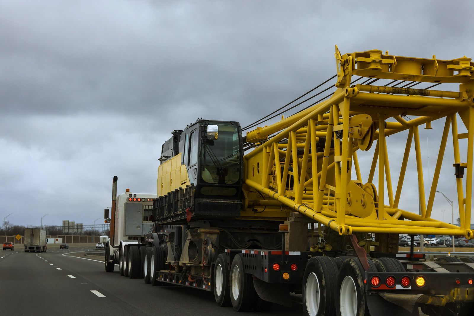 Yellow construction crane on a flatbed truck traveling on a highway under a cloudy sky