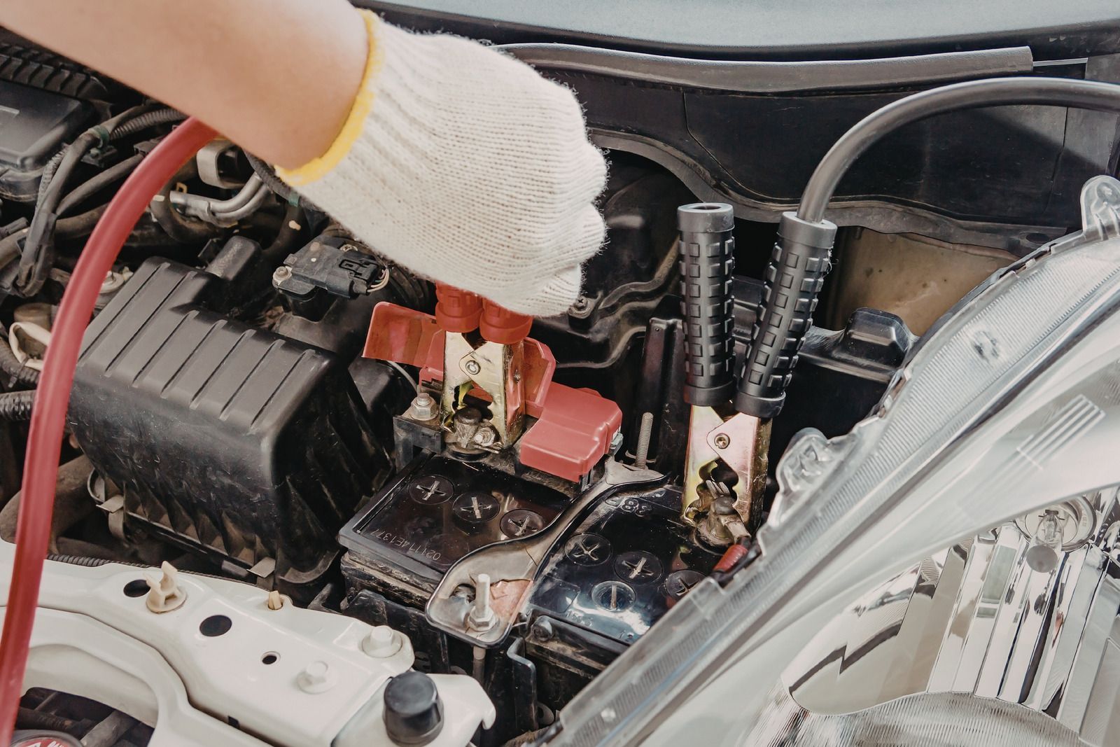 Gloved hand jump-starting a car battery in a car engine bay