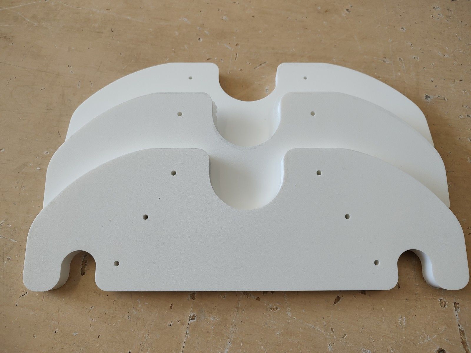 Three stacked white curved plastic parts with cutouts and holes on a cardboard surface