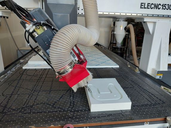 Robotic arm cutting a gray foam block on a worktable in an industrial lab