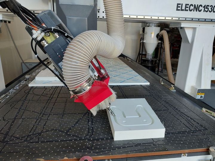 CNC router cutting a light gray panel with a red spindle and dust hose in a workshop