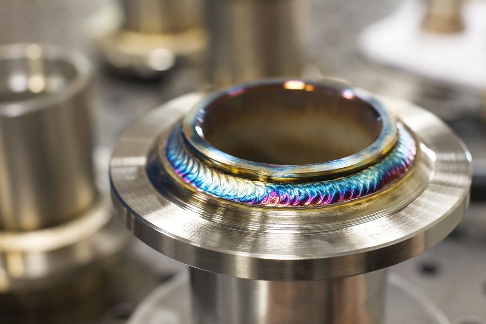 Metal pipe joint with rainbow heat discoloration on a stainless steel surface, close-up