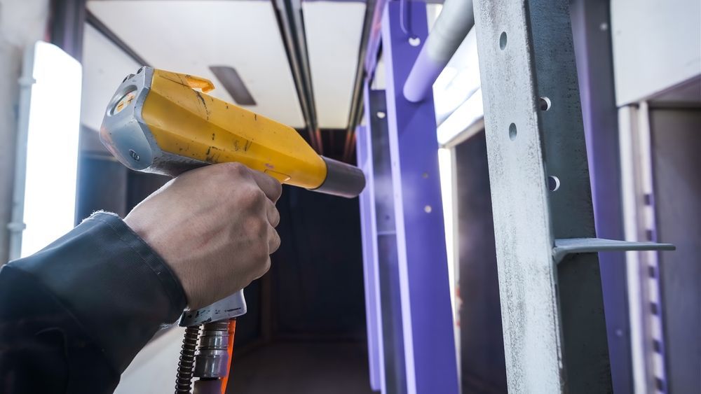 Hand holding a yellow heat gun aimed at a white door frame in a workshop or construction area
