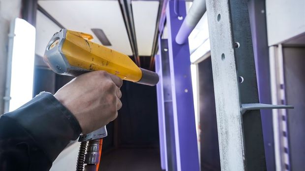 Hand holding a yellow heat gun aimed at a white door frame in a workshop or construction area