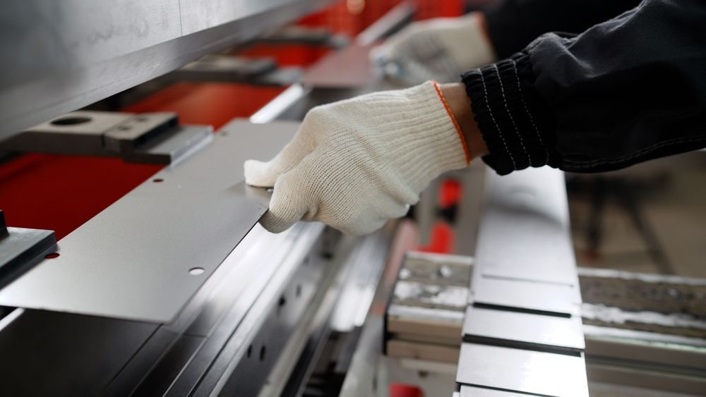 Gloved hand adjusting a metal panel on an industrial machine assembly line