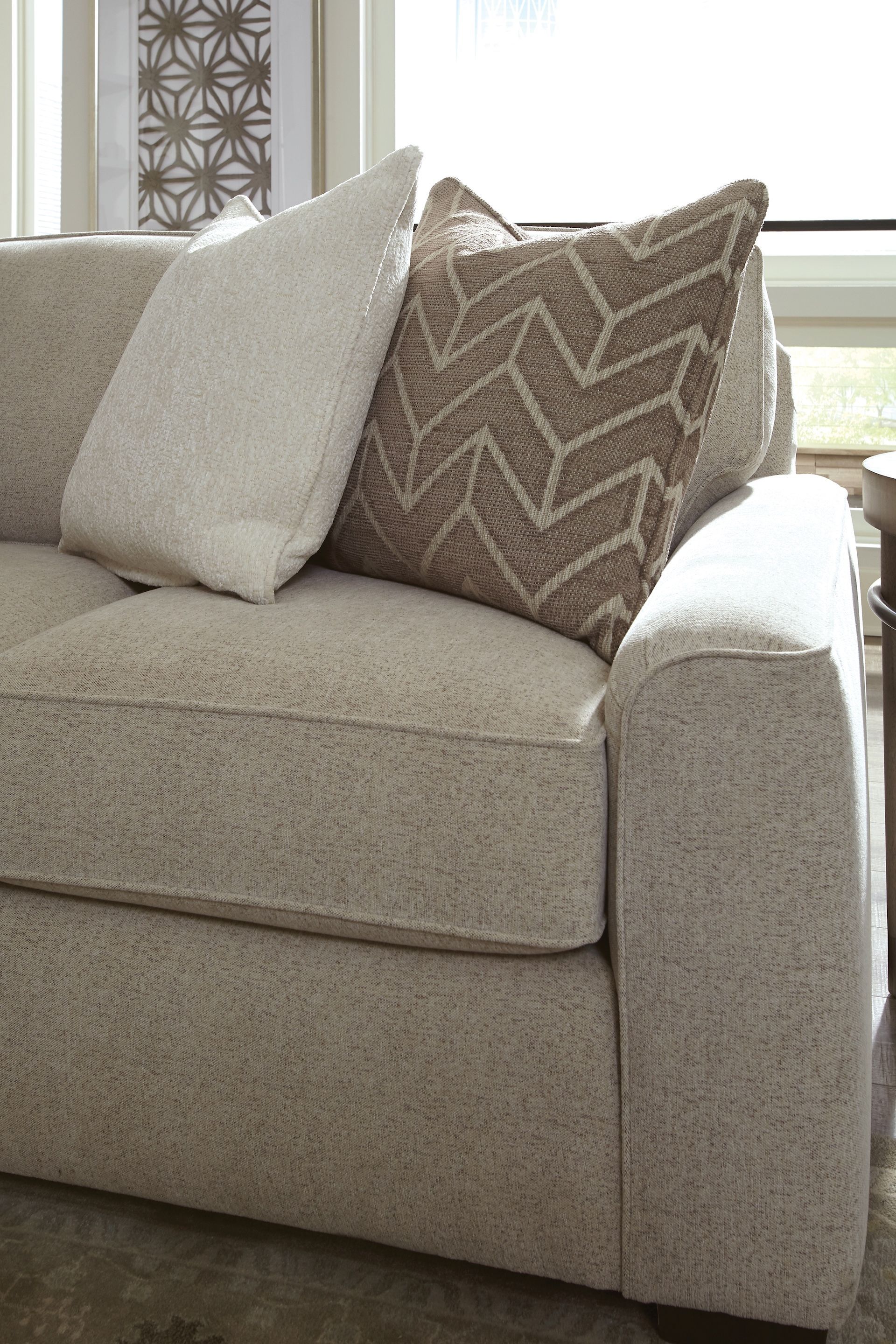 Beige sofa with two decorative pillows. One is white, the other brown with a chevron pattern.