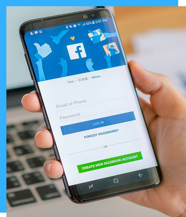 Person holding a smartphone displaying the Facebook login screen, with blue and white colors.