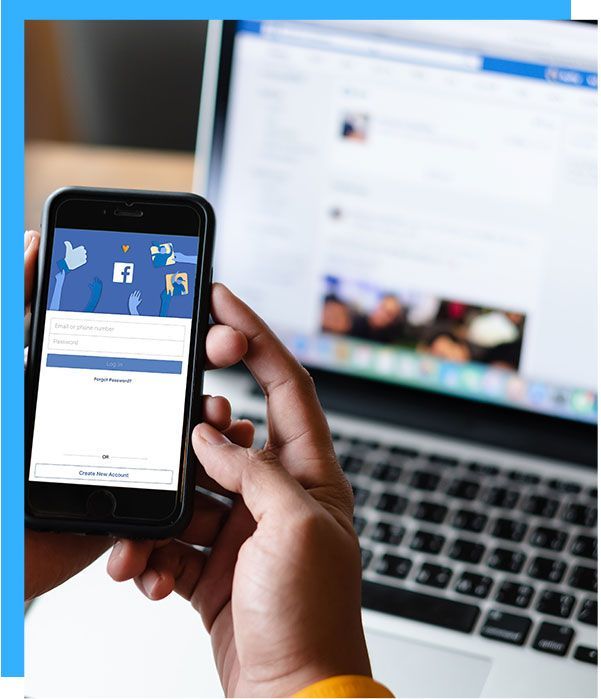 Person holding phone with Facebook app open, laptop with Facebook page in background.
