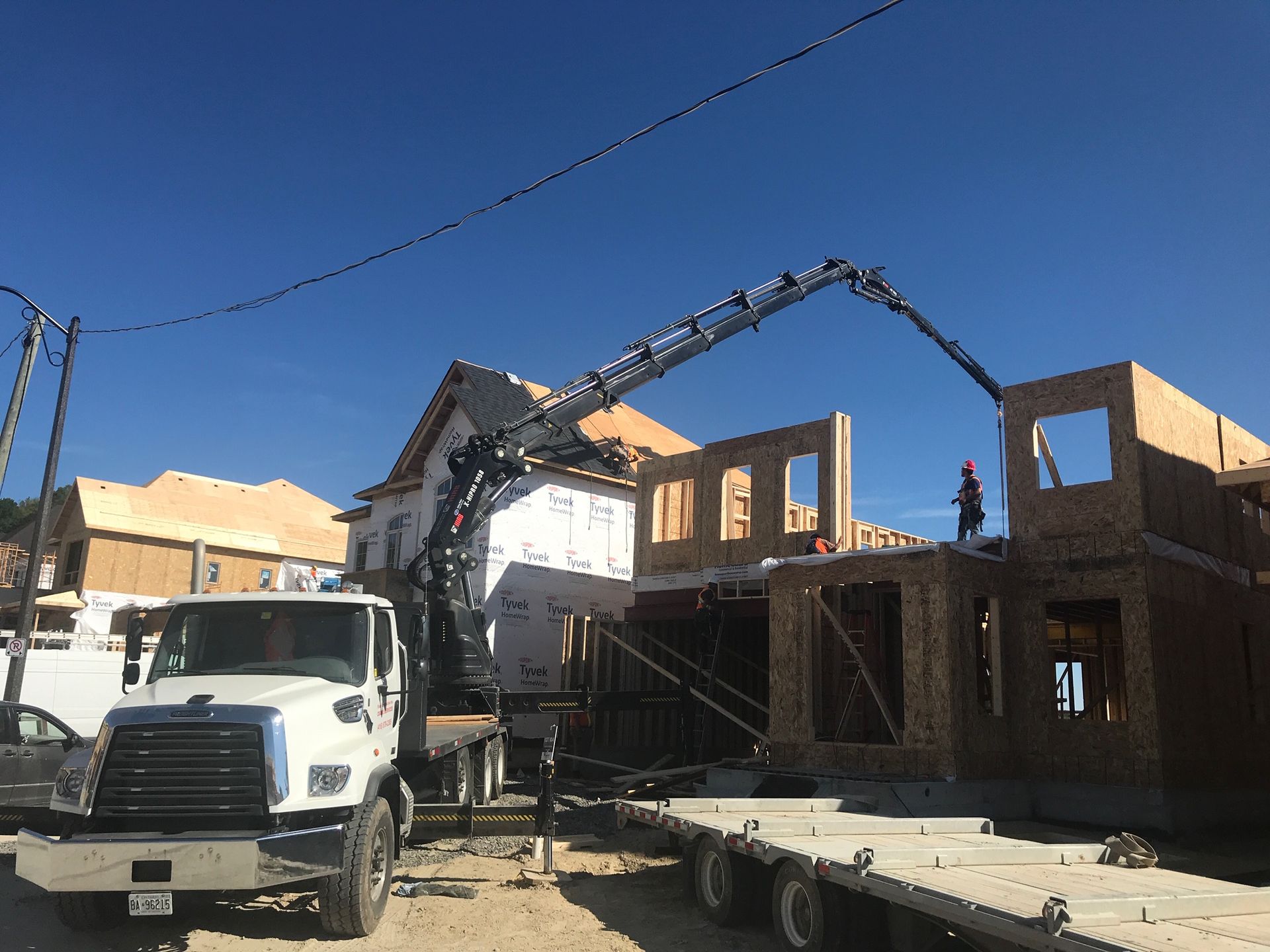 A truck with a crane attached to it is parked in front of a house under construction.