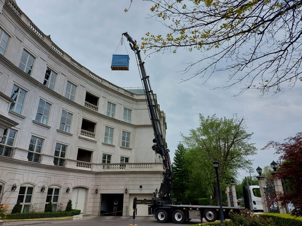 A large crane is lifting a blue box into the air in front of a large building.