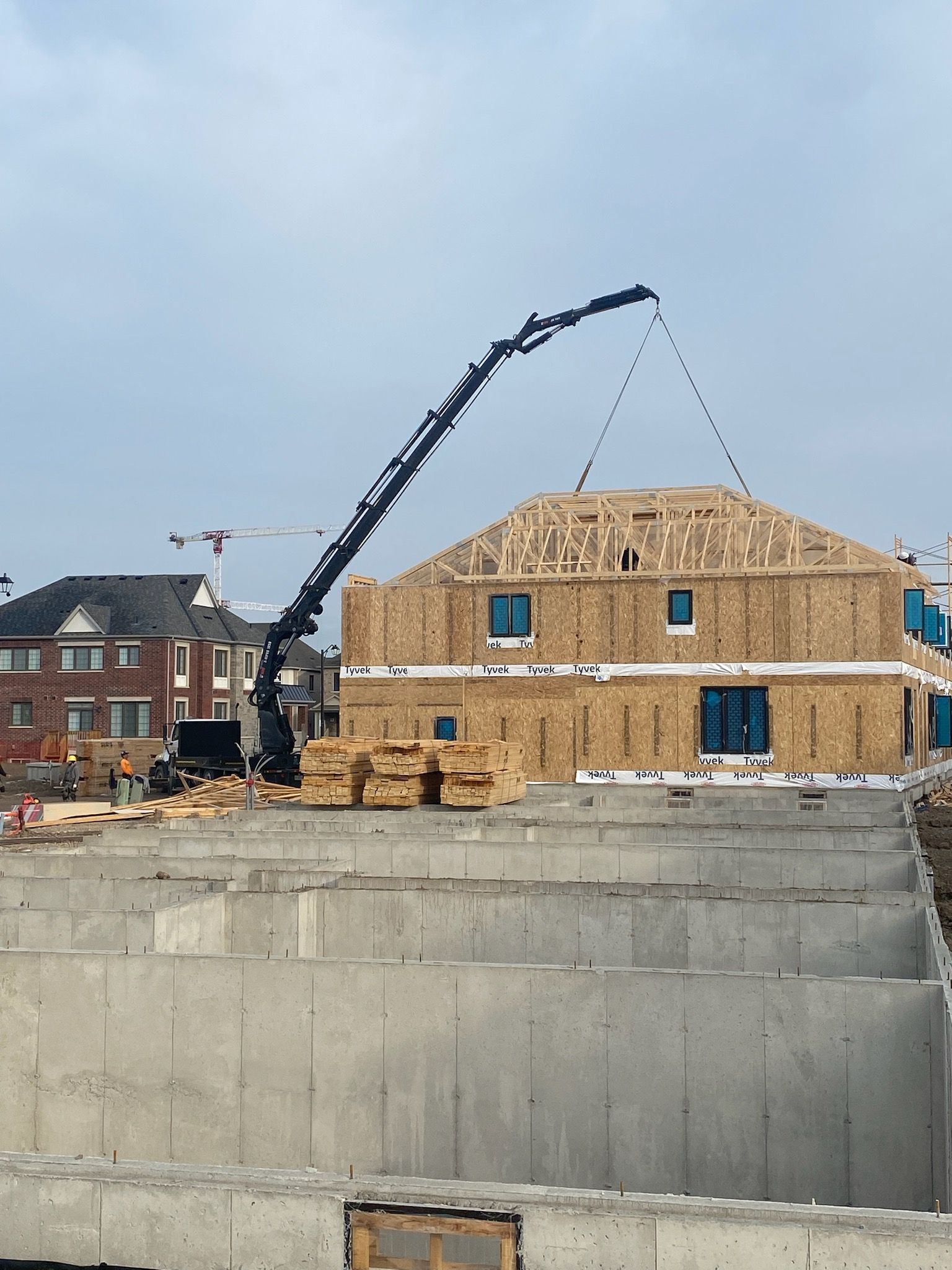 A crane is lifting a roof of a house under construction