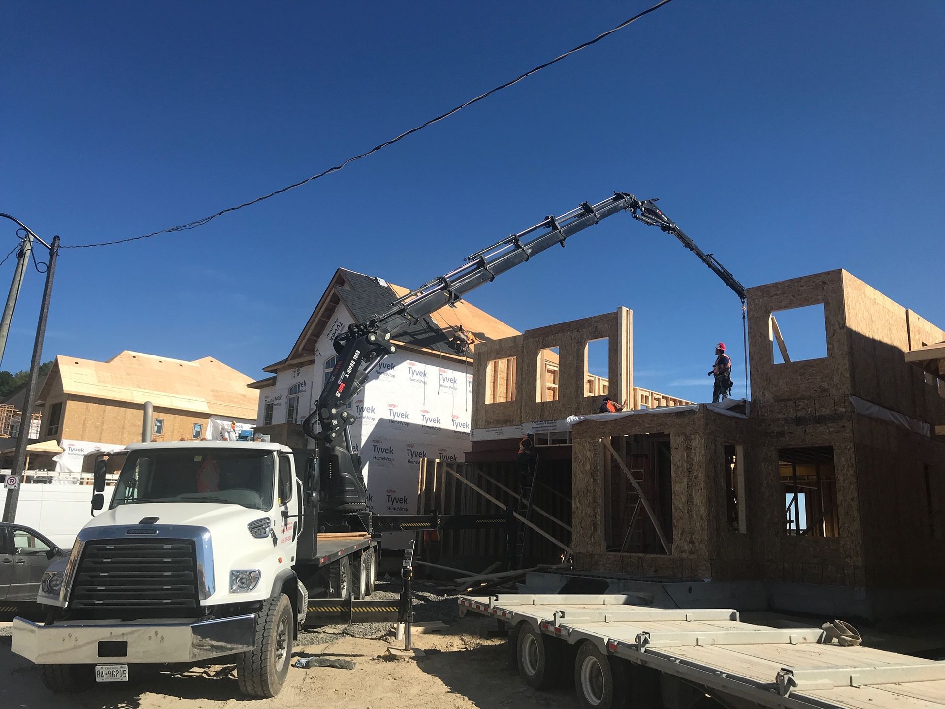 A truck with a crane attached to it is parked in front of a house under construction.