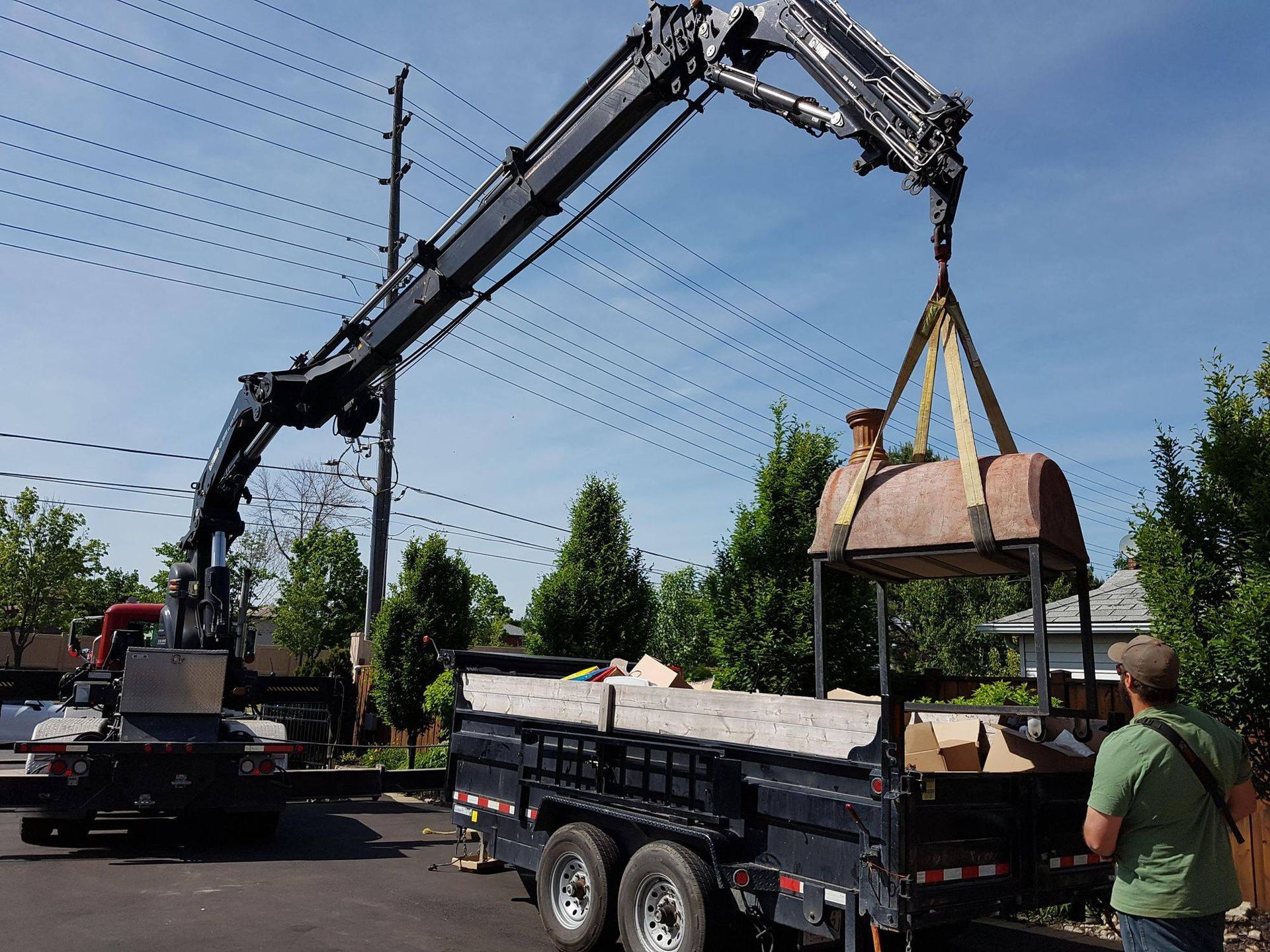 A man in a green shirt is standing in front of a dump truck with a crane attached to it