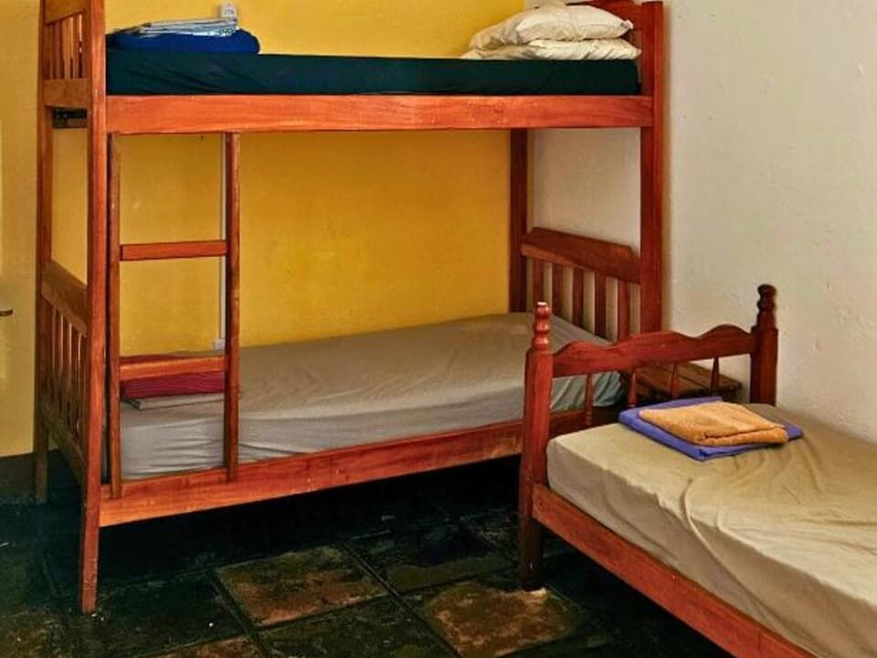 Beliche de madeira e cama de solteiro com cobertores dobrados em um pequeno quarto com paredes amarelas.