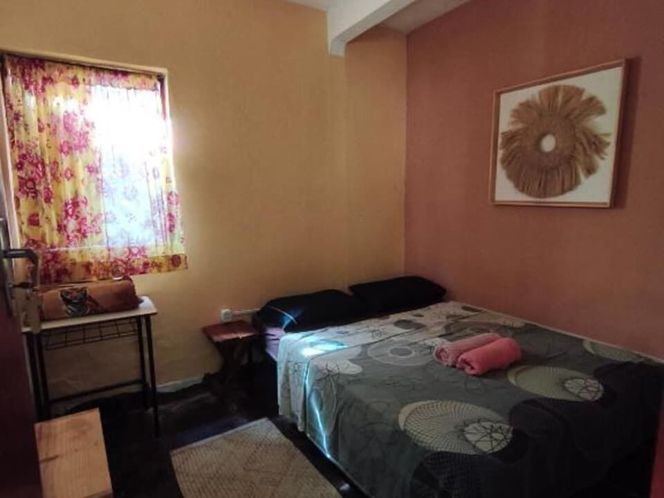 Quarto pequeno com cama, cortina floral, mesa de cabeceira e obras de arte na parede em tons quentes de laranja.