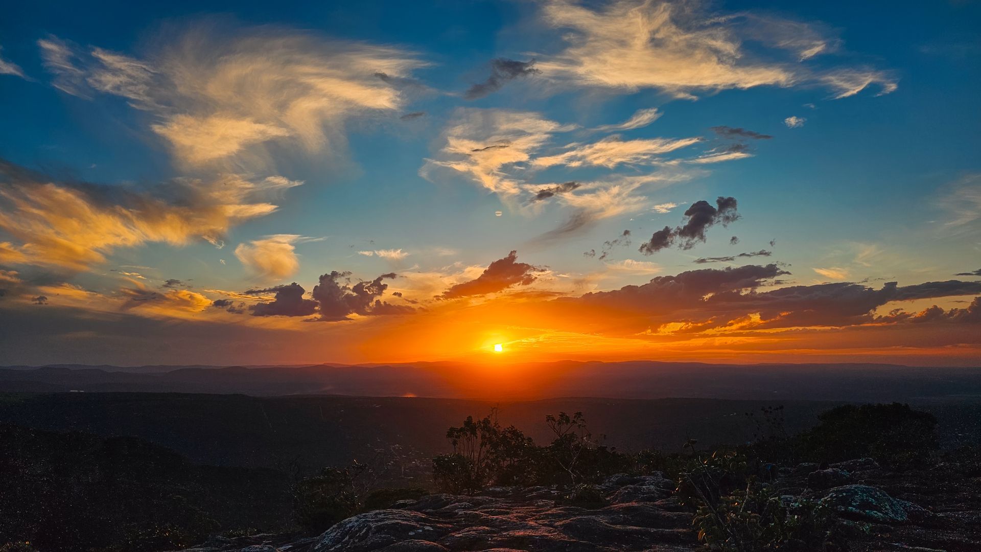 Pôr do sol sobre uma paisagem recortada com nuvens alaranjadas brilhantes e colinas escuras.